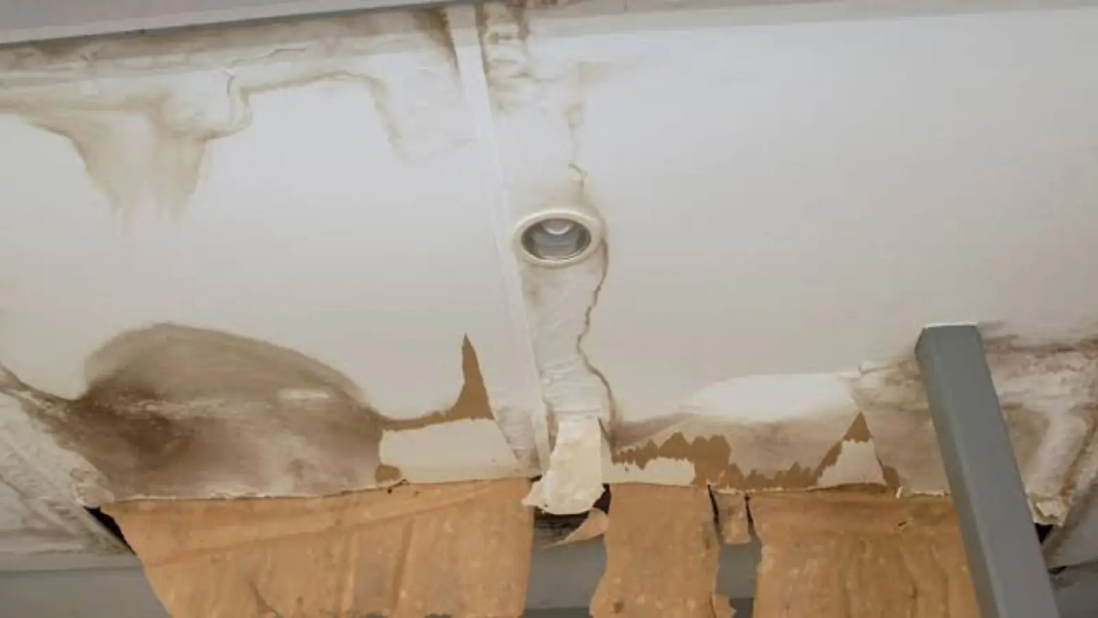 Water-stained ceiling around a recessed light with sagging, peeling drywall