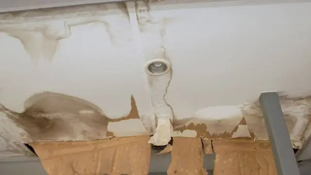 Water-stained ceiling around a recessed light with sagging, peeling drywall